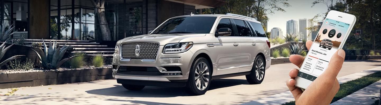 Gray Lincoln parked with Phone app showing on drivers phone standing by