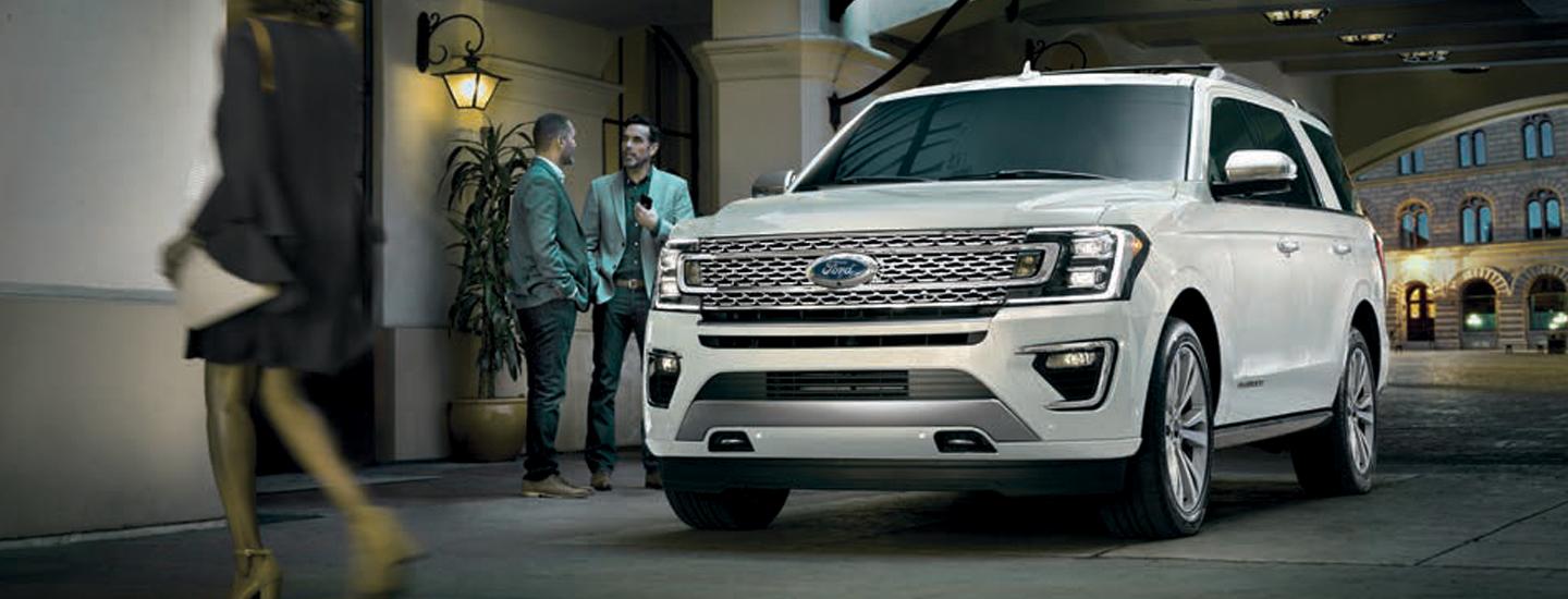 White Ford Expedition parked in front of a building next to people