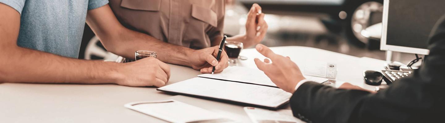 Woman and Man at desk signing papers with another man looking on