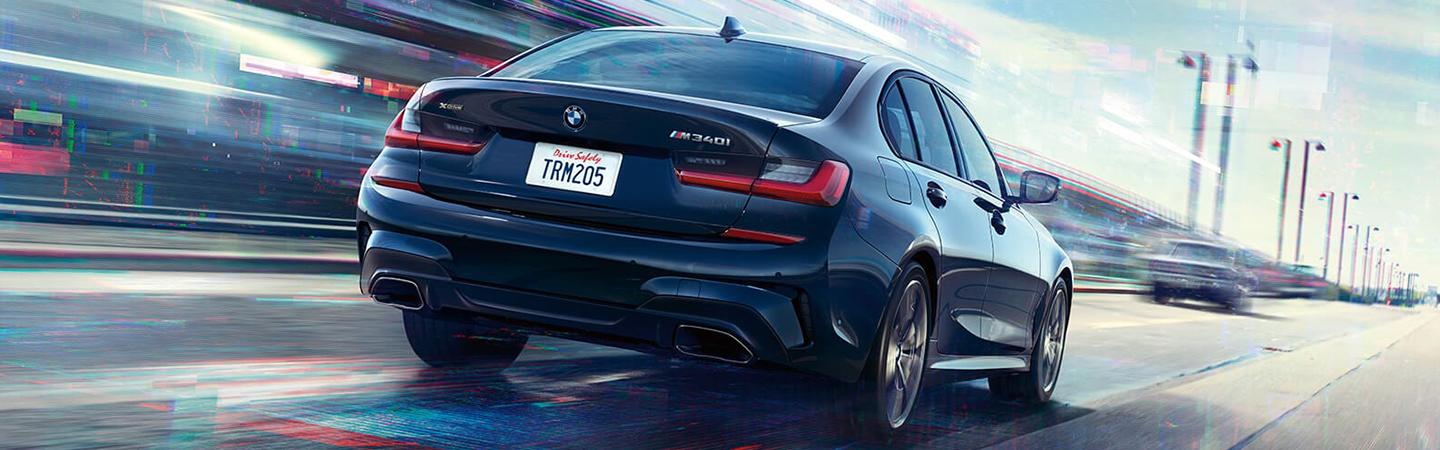 Rear view of a black BMW 3 Series driving down the road.