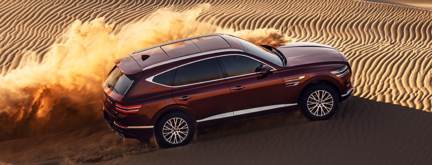 Top view of a red Genesis GV80 driving over a sand dune.