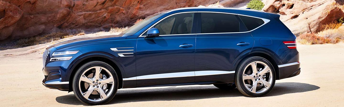 Side view of a blue Genesis GV80 parked near red desert rocks.