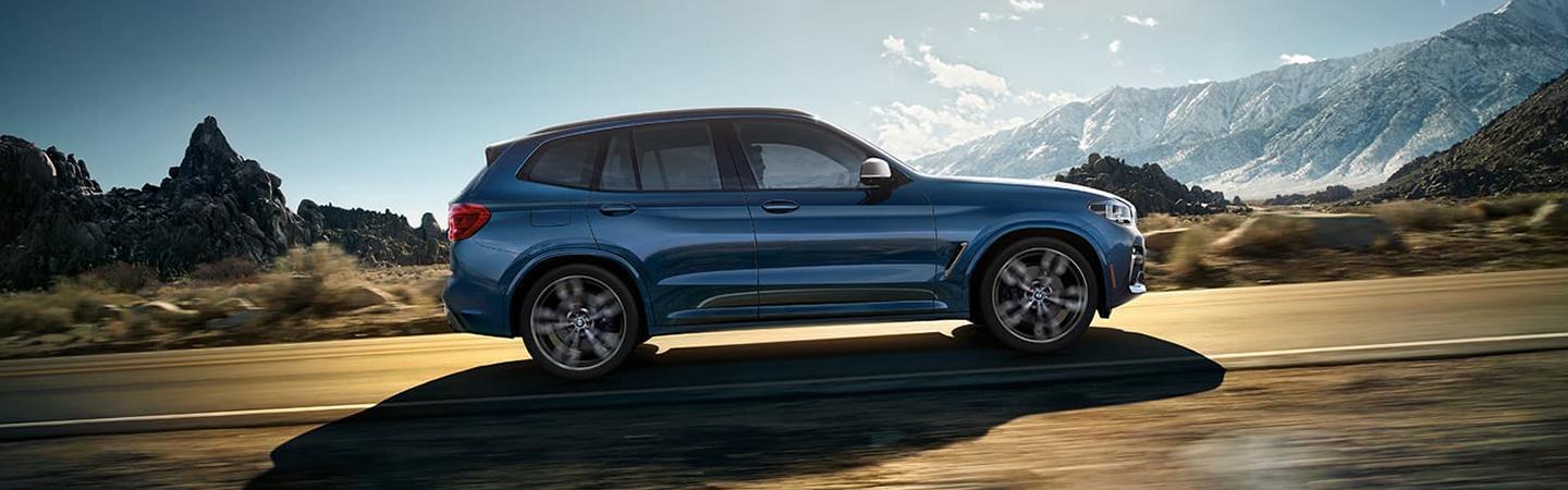 Side view of a blue BMW X3 driving through the mountains.