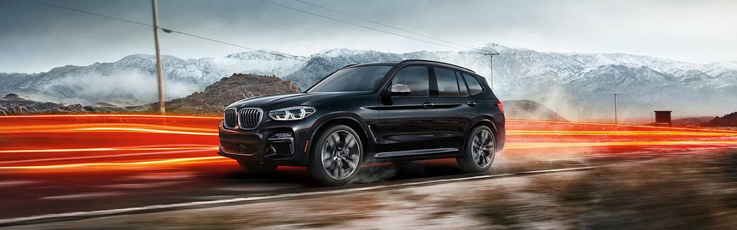 Side view of a black BMW X3 racing along the road.