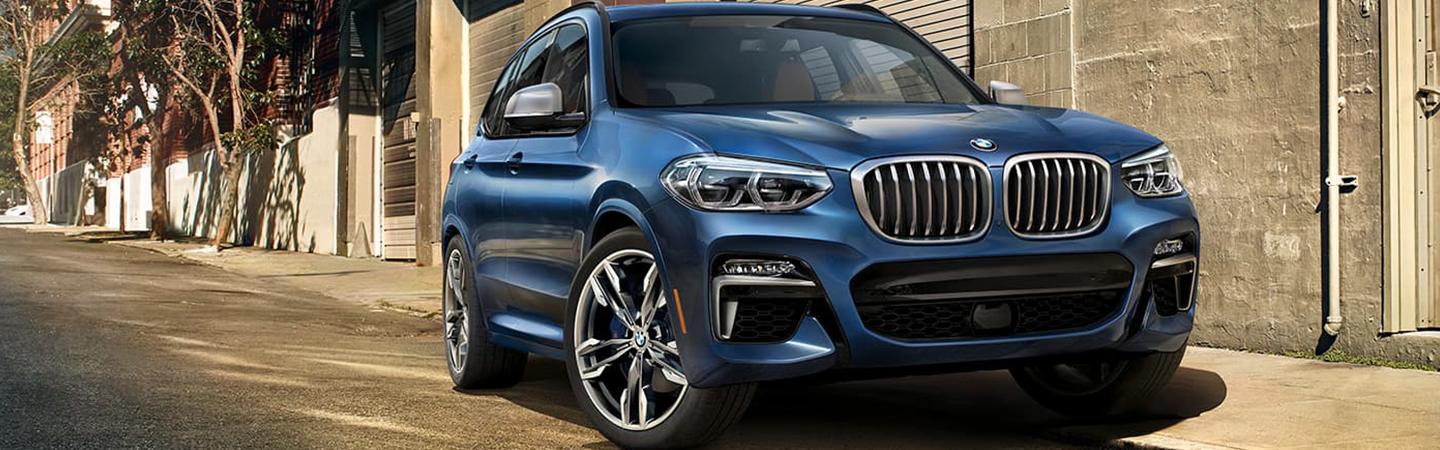 Front view of a blue BMW X3 parked next to a building.