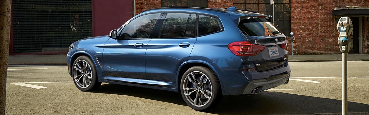Rear view of a blue BMW X3 parked along a city street.