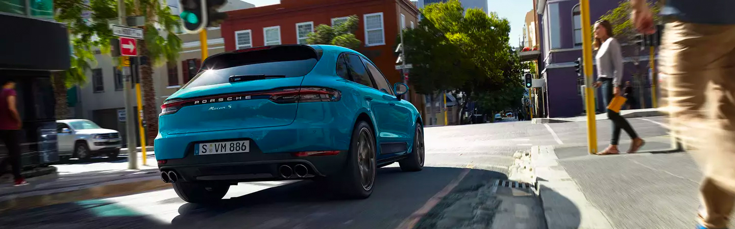 Rear view of an aqua blue 2020 Porsche Macan driving through the city