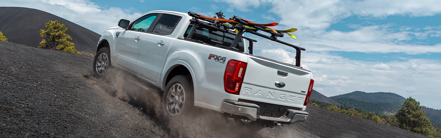 Rear view of a white 2020 Ford Ranger driving uphill on a dirt road 