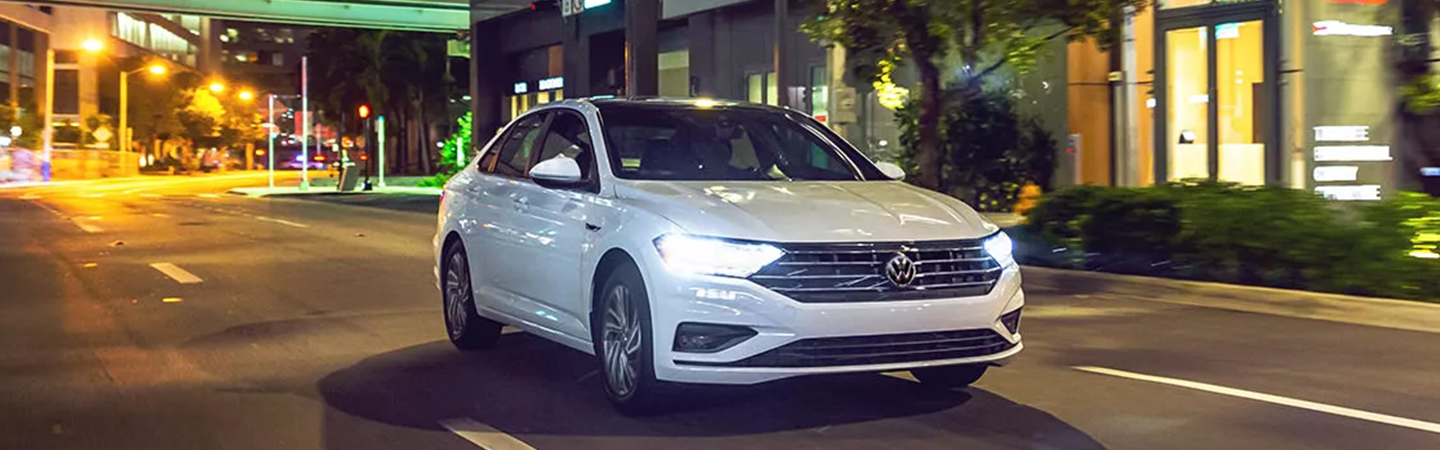 White 2021 Volkswagen Jetta driving with headlights on
