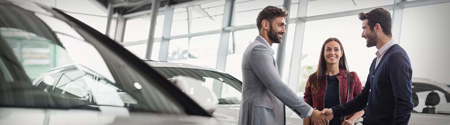 Man shaking hands with another man with woman in dealership