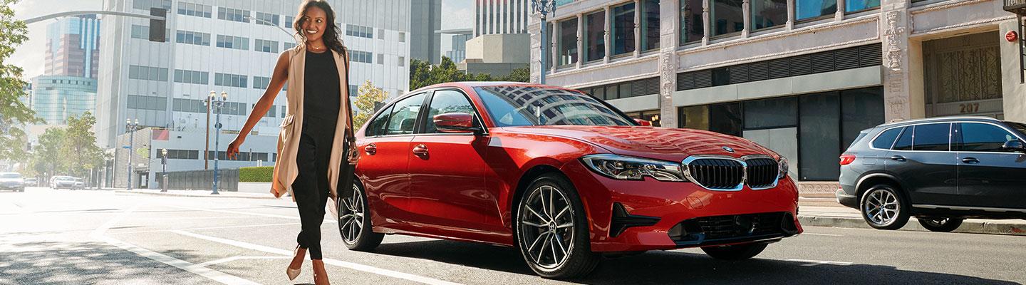 Woman walking away from a red BMW 3 Series parked on the city street.