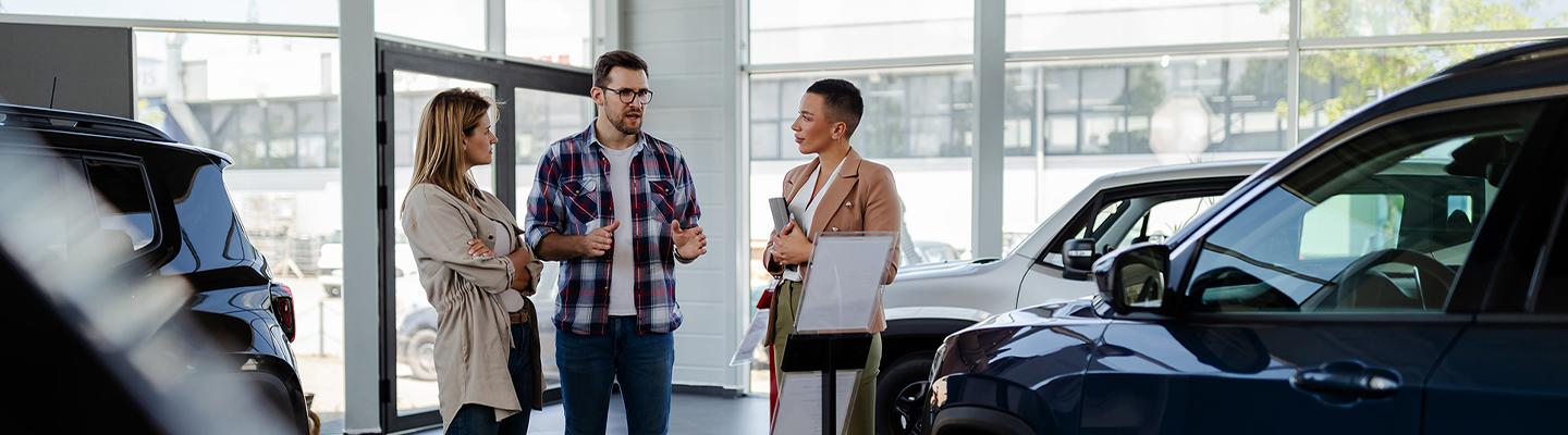 Woman and man speaking with car sales person in showroom