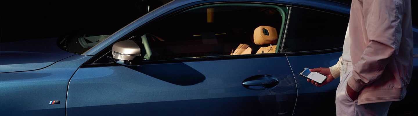 A person using their iPhone to unlock their blue BMW sedan.