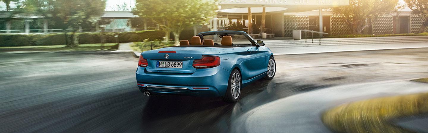 Rear view of a blue convertible BMW 2 Series driving down the road.