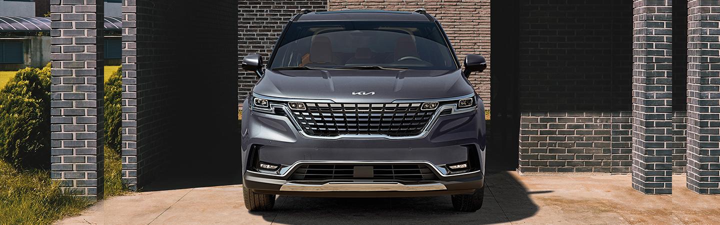 Front view of a grey Kia Carnival parked near a building.