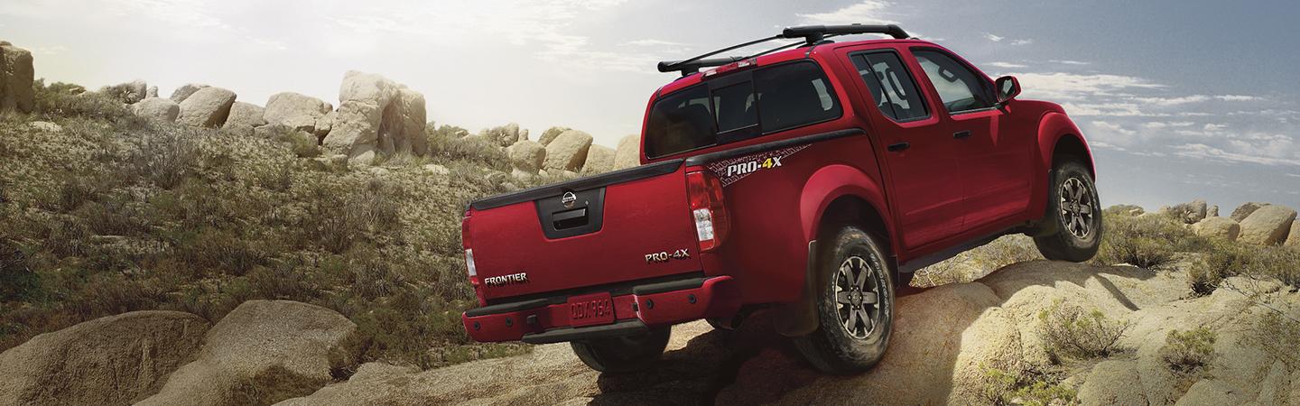 Rear view of a red Nissan Frontier climbing boulders.