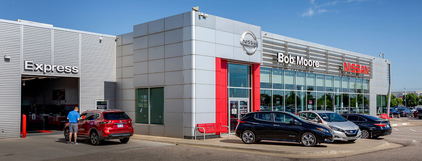 Bob Moore Nissan dealership with scarlet ember Nissan Rogue sitting in front of service center garage.