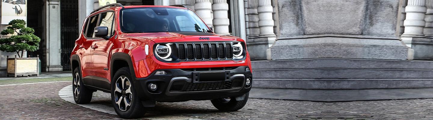 A Red Jeep Renegade parked in front of old stone building.