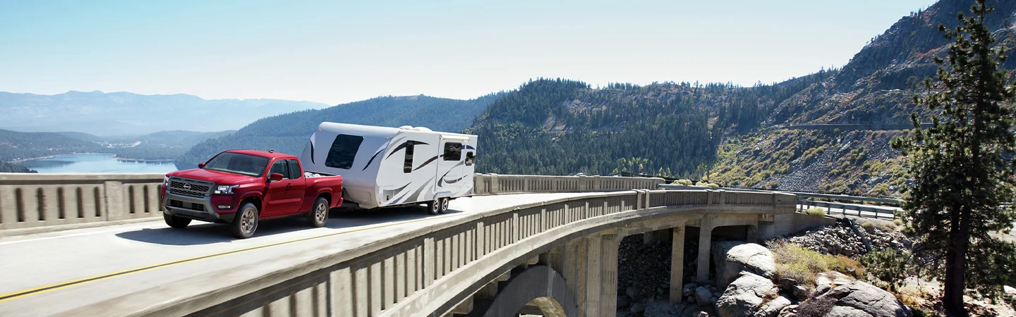 2025 Nissan Frontier SL driving on a bridge towing a camper