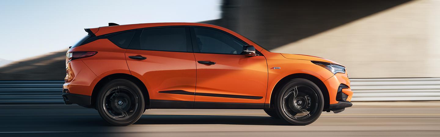 Side profile of an orange 2022 Acura RDX in motion