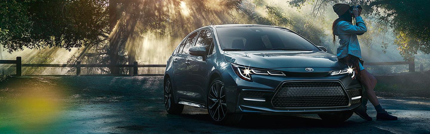 Woman leaning on 2020 Toyota Corolla in the forest