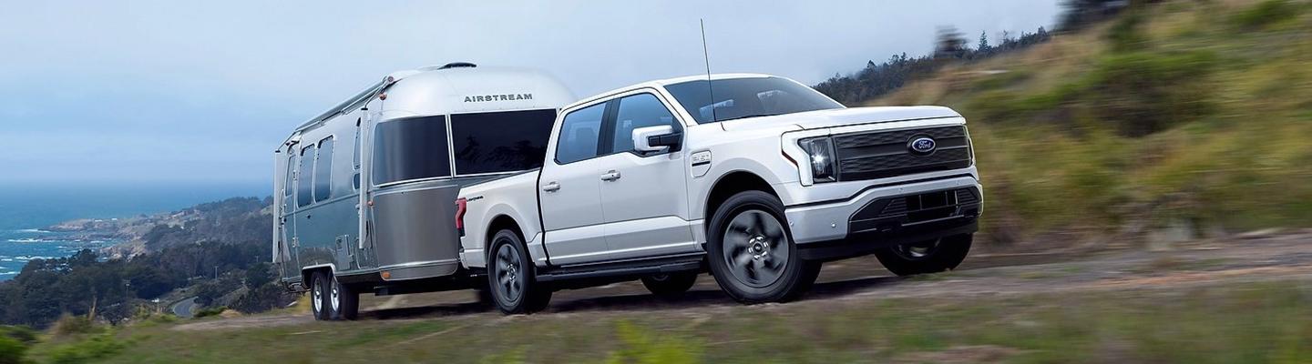 Angled profile of a white Ford F-150 Lightning towing a trailer uphill