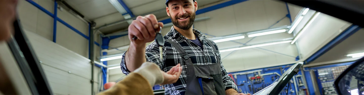 Auto mechanic handing keys to someone in a car