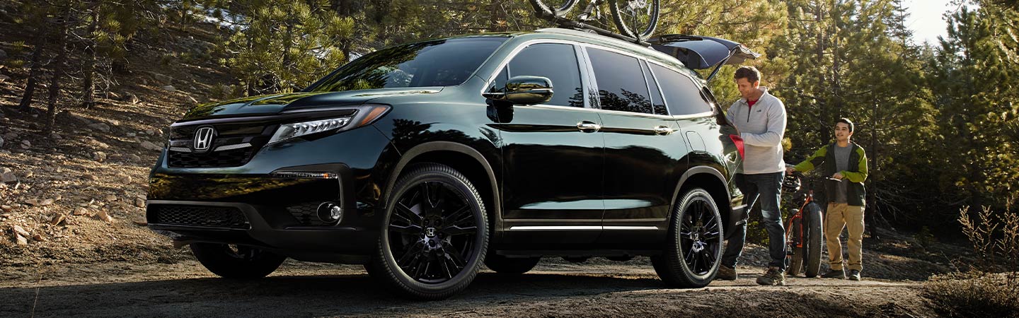Black Honda Pilot parked; driver loading cargo in the back.