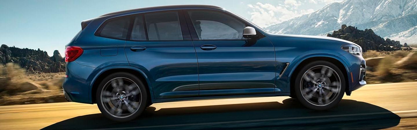 2021 BMW X3 in motion passenger side view driving in mountain valley