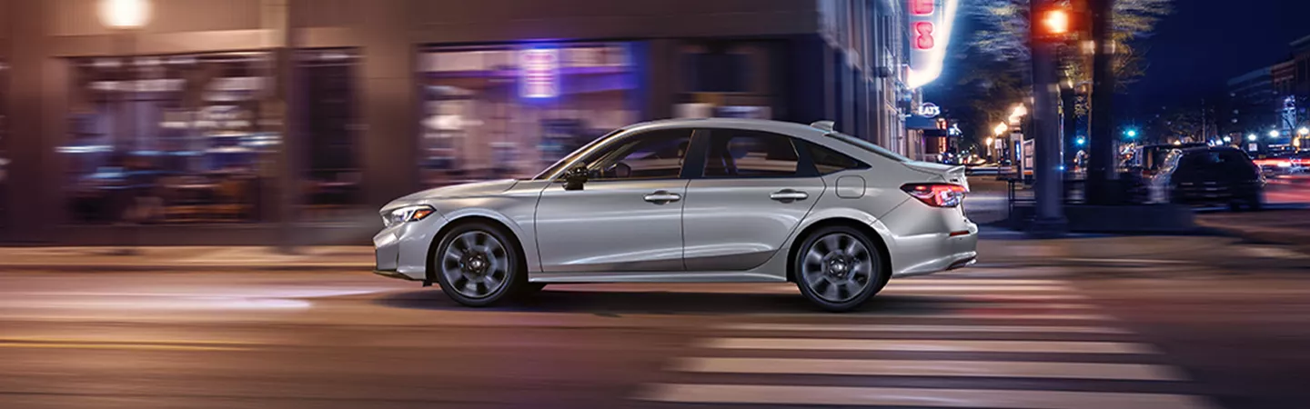 Side view of the 2026 Honda Civic driving through the city at night with lights